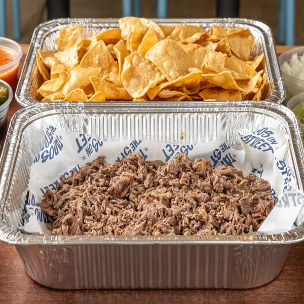 Two foil trays of Tacos On The Street catering, one with tortilla chips and one with shredded meat.