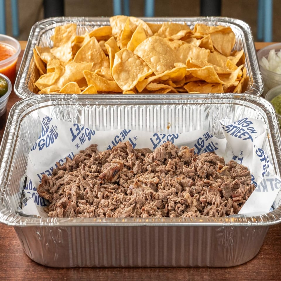 Two foil trays of Tacos On The Street catering, one with tortilla chips and one with shredded meat.